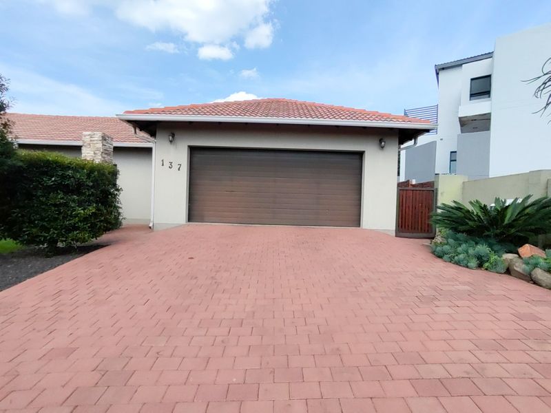 Front view of the property featuring a paved driveway leading to a double garage with a tiled roof and side gate access.