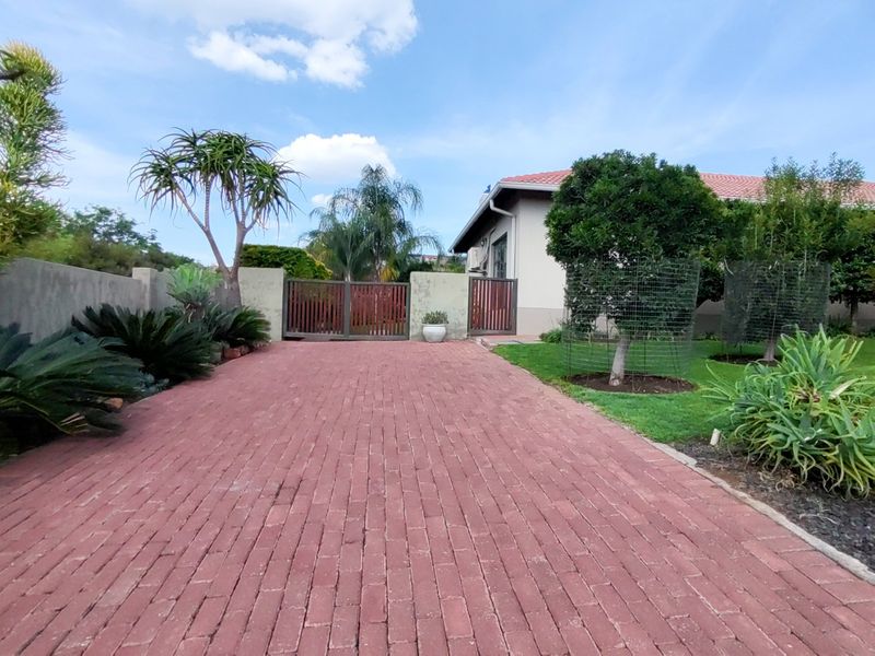 A well-maintained front exterior featuring a red brick paved driveway, secure timber gate access, and established garden landscaping.