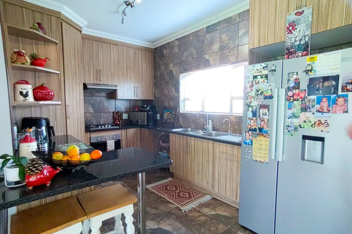 A functional kitchen featuring wood-finish cabinetry, granite countertops, a built-in oven with gas hob, and tiled finishes throughout.