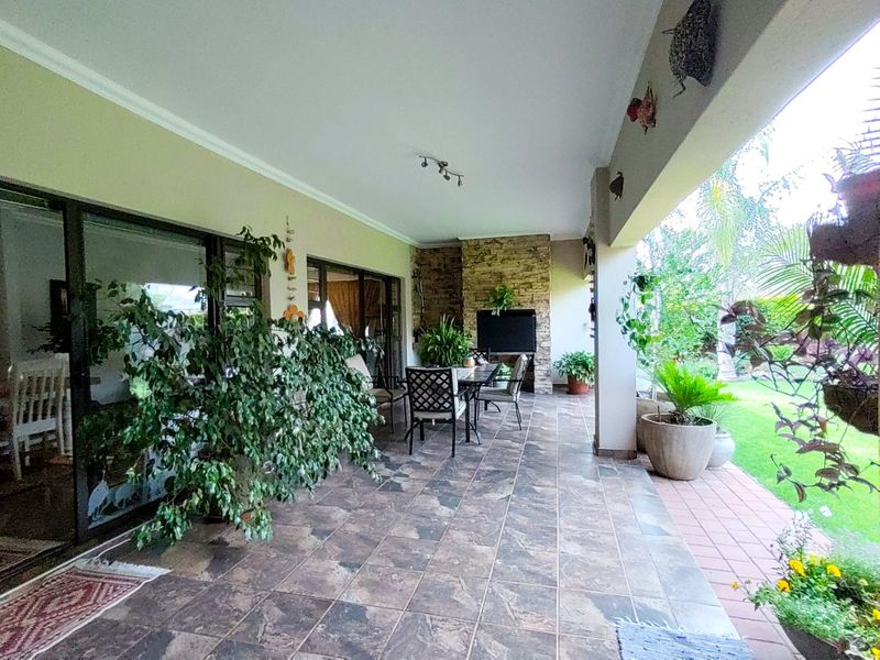 Spacious covered patio featuring tiled flooring, a built-in fireplace with stone cladding, and large sliding glass doors leading to the garden.
