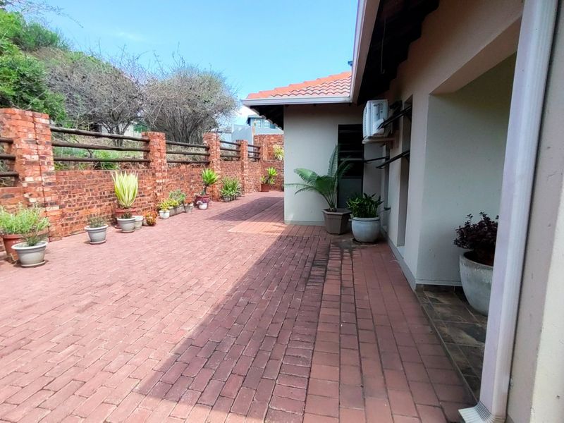 A paved outdoor patio area featuring a brick boundary wall and an external air conditioning unit, providing a functional space for outdoor living.