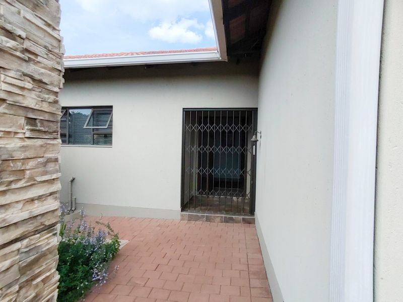 A rear exterior view featuring a paved patio area, stone-clad pillar, and a secure entrance with a metal security gate.