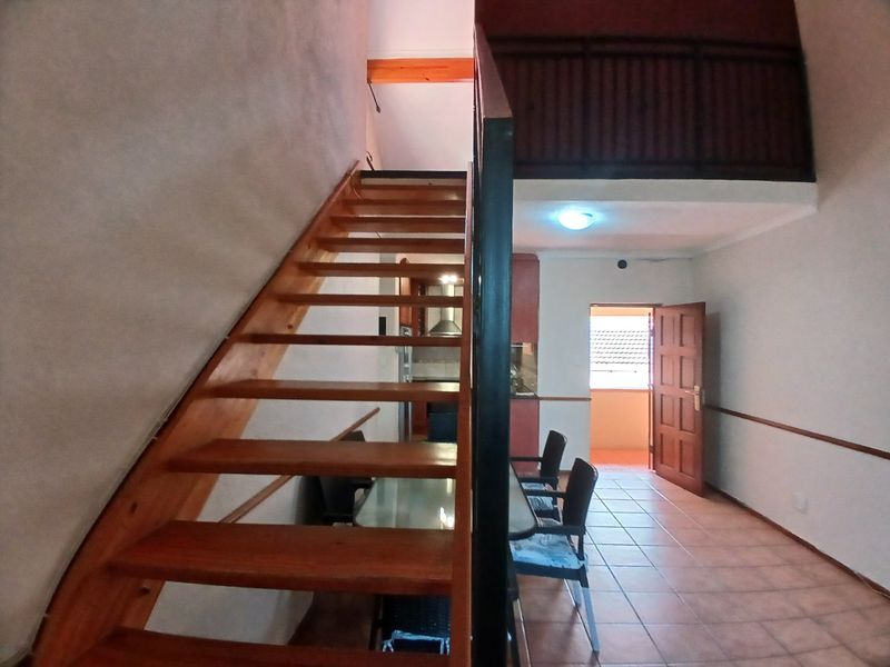 Open plan living area featuring a wooden staircase leading to a mezzanine level, tiled flooring, and access to an exterior balcony.