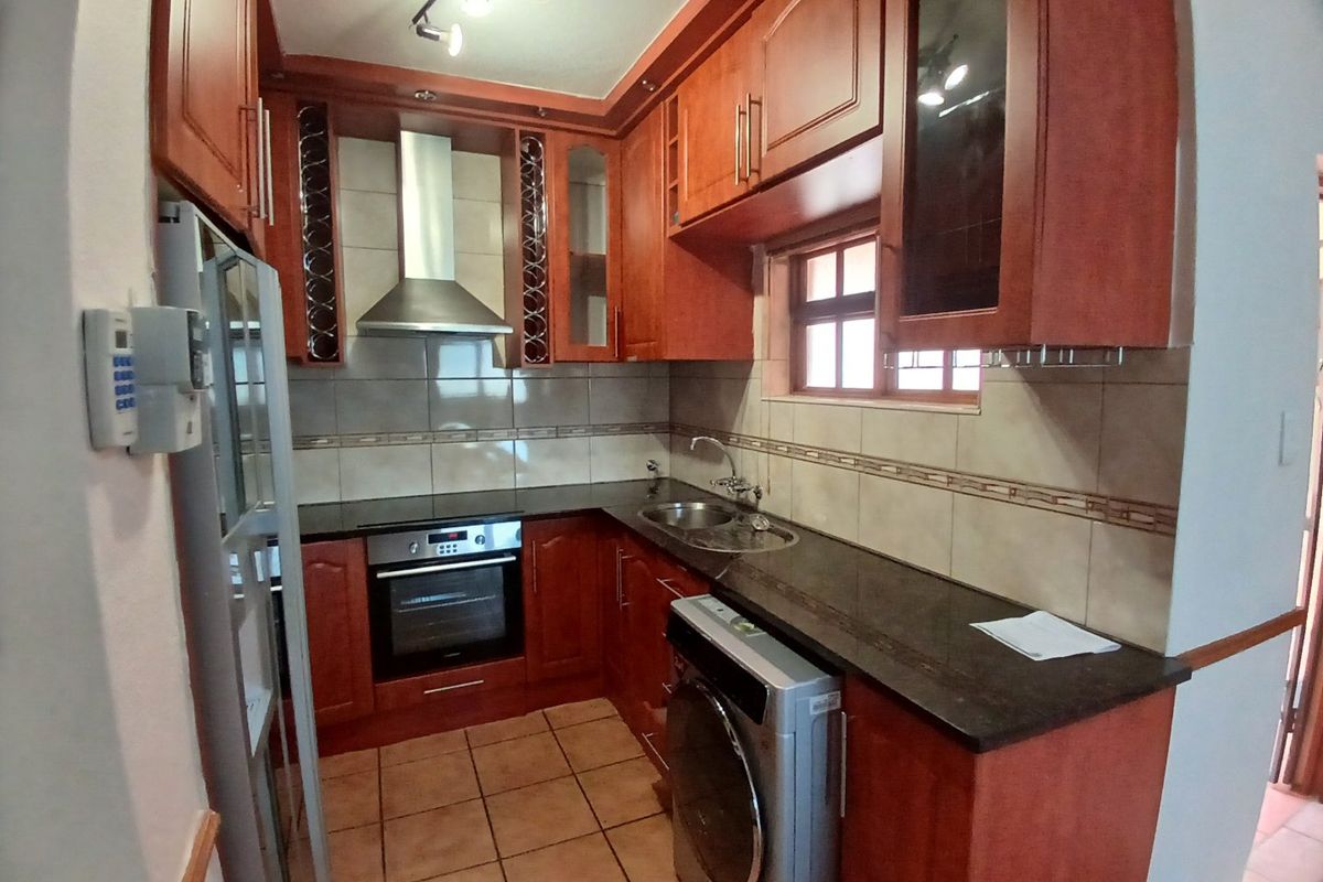 A functional kitchen featuring warm-toned wooden cabinetry, granite countertops, a built-in oven, and a stainless steel extractor fan with tiled backsplash and flooring.
