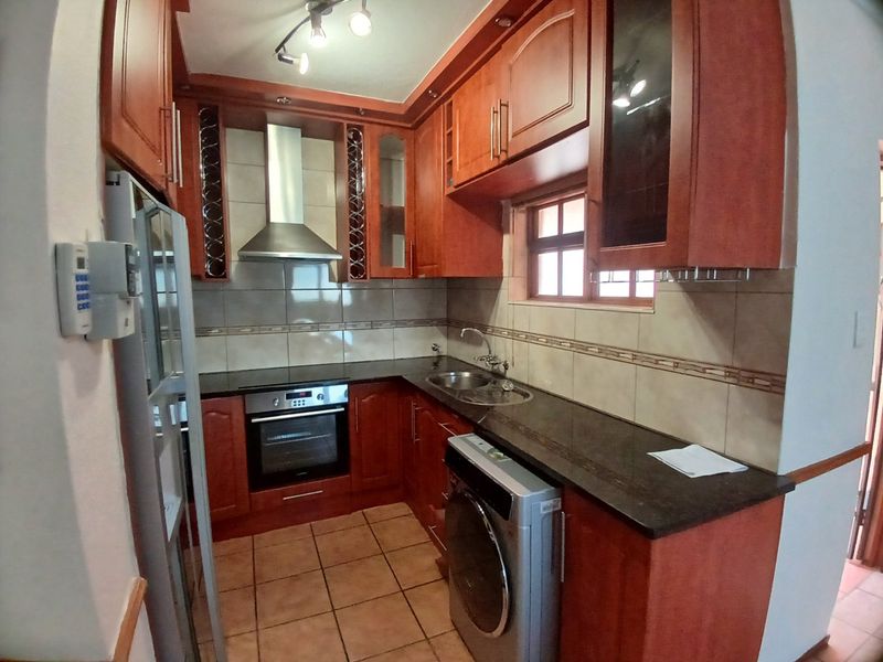 A functional kitchen featuring warm-toned wooden cabinetry, granite countertops, a built-in oven, and a stainless steel extractor fan with tiled backsplash and flooring.