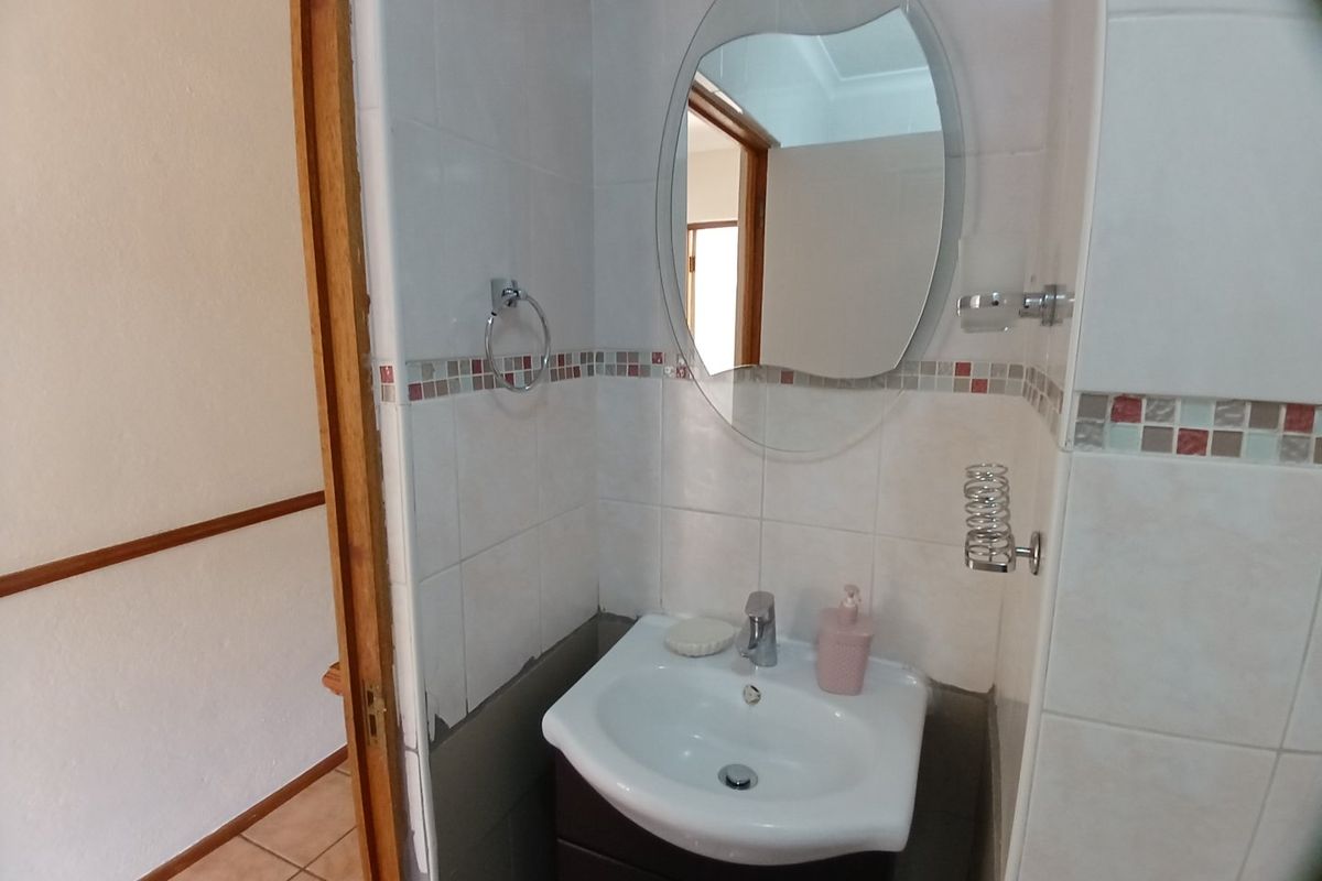 A compact bathroom featuring a vanity basin, wall-mounted mirror, and tiled walls with decorative mosaic accents.