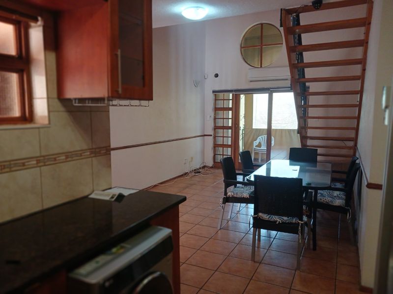 Open plan living and dining area featuring tiled floors, a wooden staircase, and direct access to a balcony through sliding glass doors.