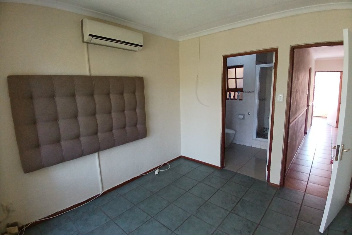 A bedroom featuring tiled flooring, an air conditioning unit, and direct access to an en-suite bathroom and hallway.