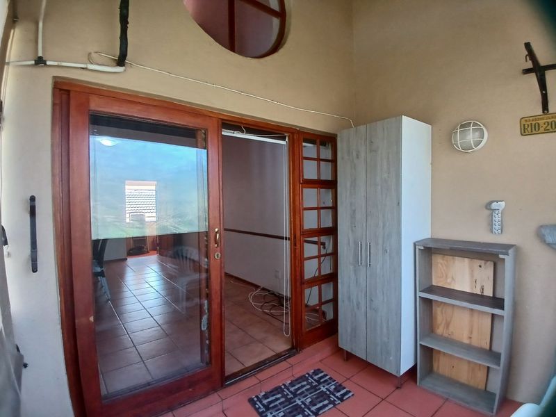 A covered balcony area featuring tiled flooring, a wooden sliding door entrance, and high-level architectural window detail.