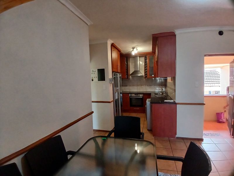 Open plan kitchen and dining area featuring wooden cabinetry, built-in oven, extractor fan, and tiled flooring with access to an outdoor balcony.