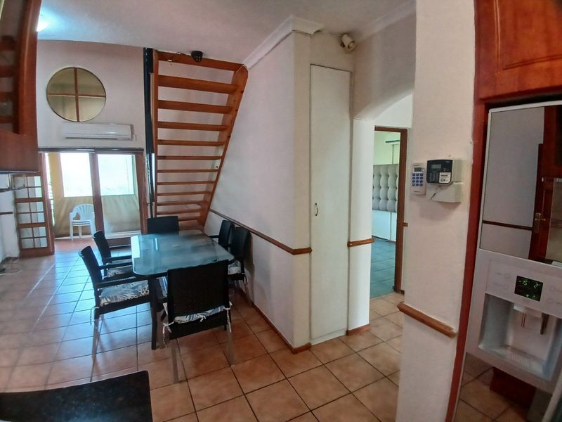 Open plan living and dining area featuring a wooden staircase, tiled flooring, and access to an outdoor patio through sliding glass doors.