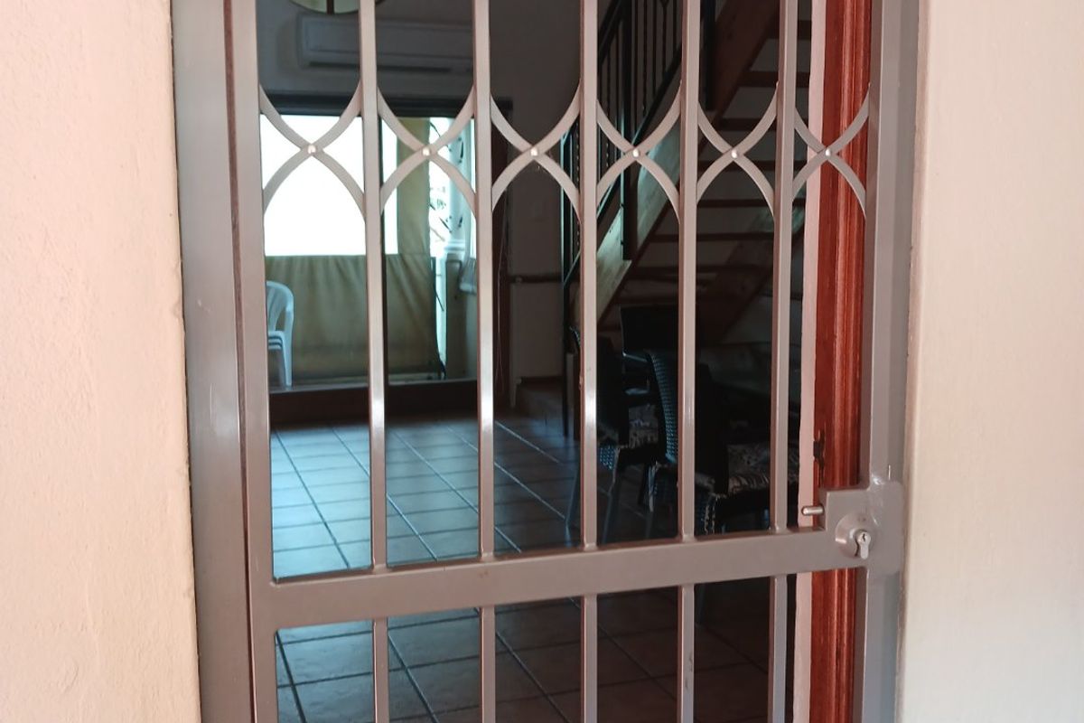 View through a security gate into an entrance area featuring tiled flooring, a staircase, and an air conditioning unit.