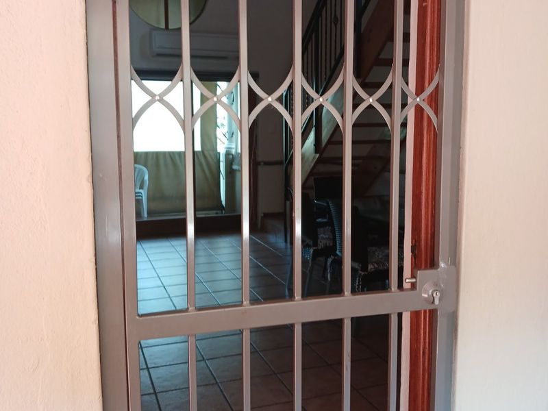 View through a security gate into an entrance area featuring tiled flooring, a staircase, and an air conditioning unit.