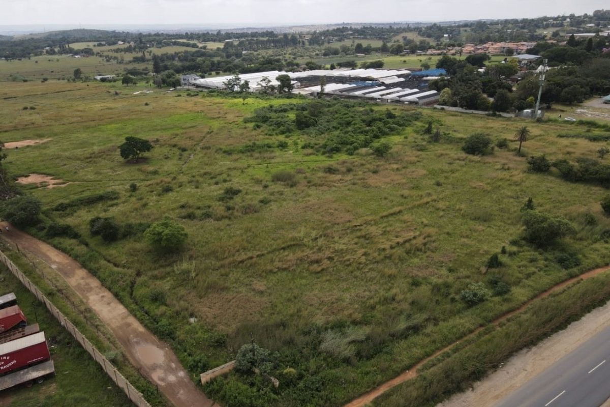 An aerial view of a large, undeveloped residential plot featuring natural vegetation, perimeter fencing, and adjacent road access.