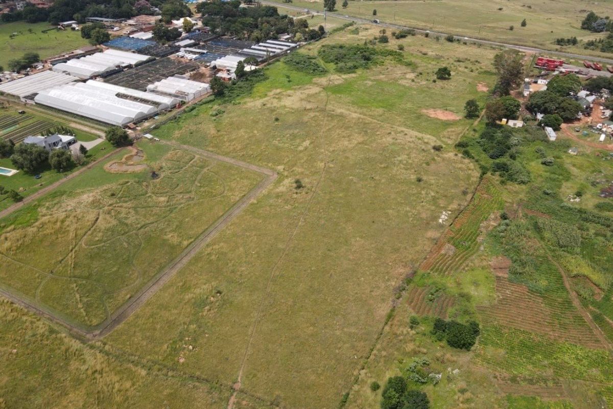 An aerial view of a large, undeveloped residential plot of land featuring open grassland and proximity to local agricultural and commercial areas.