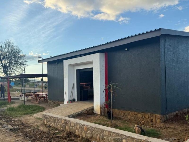 Rear view of a commercial building featuring a dark textured facade, stone base, concrete entrance ramp, and a separate built-in outdoor braai area.