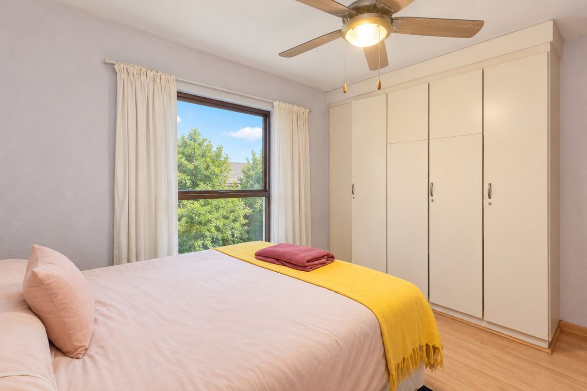 A well-maintained bedroom featuring laminate flooring, a ceiling fan, and ample built-in cupboard storage with natural light from the window.