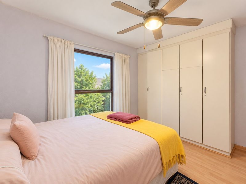 A well-maintained bedroom featuring laminate flooring, a ceiling fan, and ample built-in cupboard storage with natural light from the window.