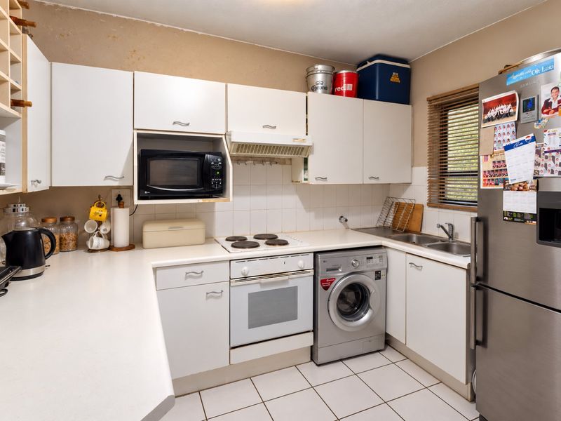Functional kitchen featuring white cabinetry, built-in oven and hob, tiled backsplash, and integrated laundry appliance space.