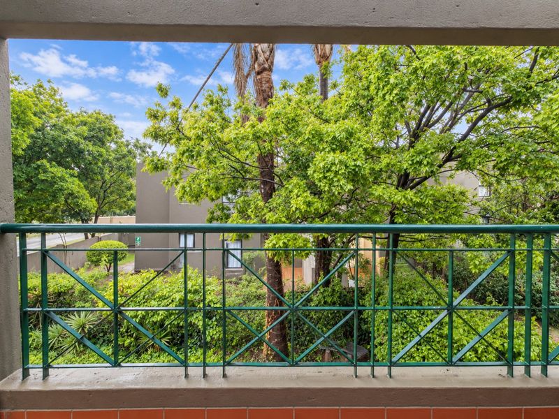 A private balcony featuring a green metal balustrade with views overlooking the surrounding garden and complex grounds.