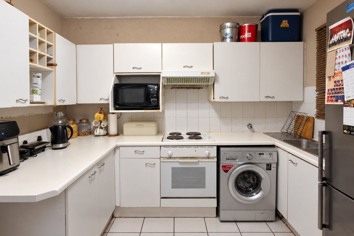 A functional kitchen featuring white cabinetry, built-in oven, electric hob, extractor fan, and tiled flooring, offering a practical layout for daily meal preparation.