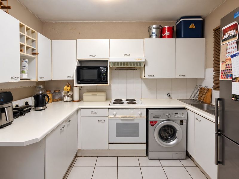 A functional kitchen featuring white cabinetry, built-in oven, electric hob, extractor fan, and tiled flooring, offering a practical layout for daily meal preparation.