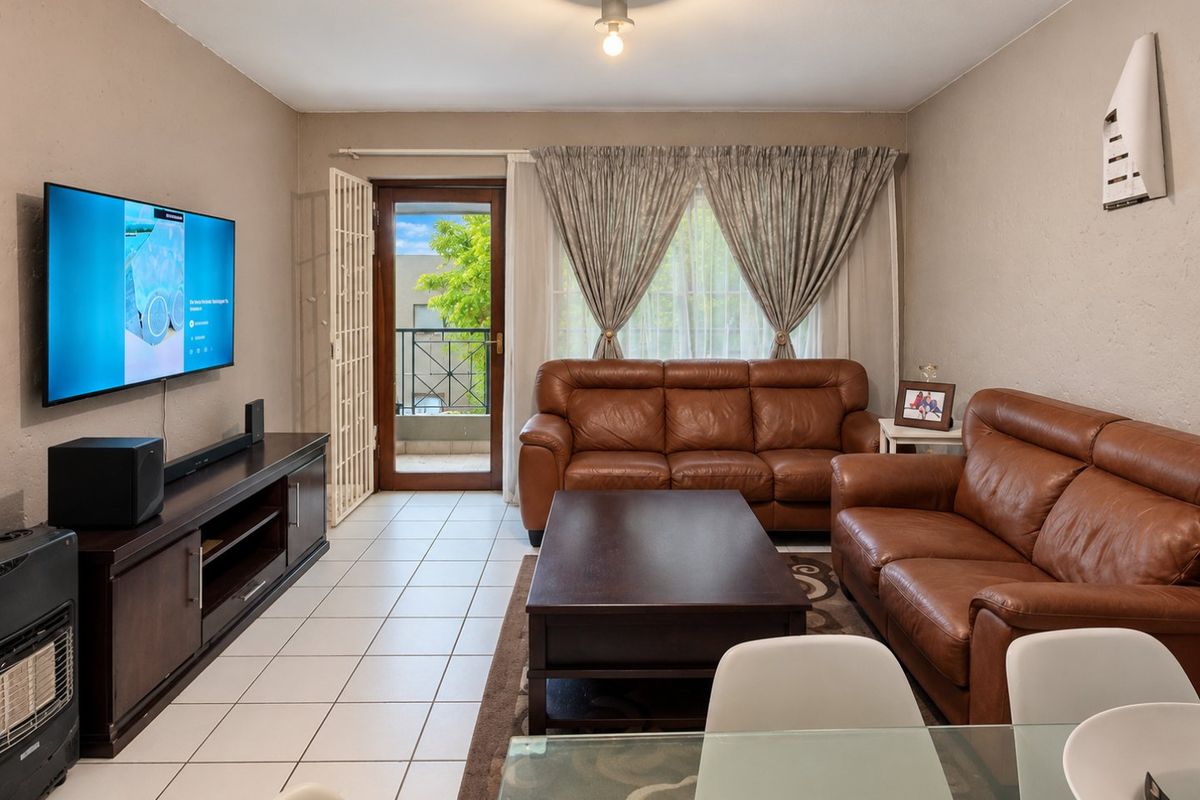A well-lit living room featuring tiled flooring, a wall-mounted air conditioning unit, and direct access to a private balcony through a glass door.
