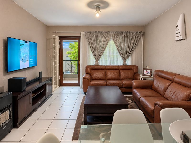 A well-lit living room featuring tiled flooring, a wall-mounted air conditioning unit, and direct access to a private balcony through a glass door.