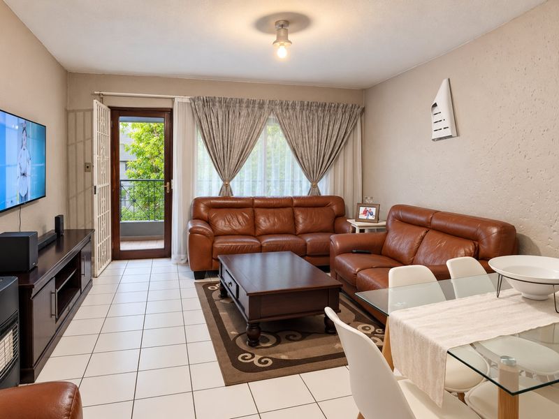 Open-plan living and dining area featuring tiled flooring, a wall-mounted heater, and direct access to a private balcony through a secure glass door.