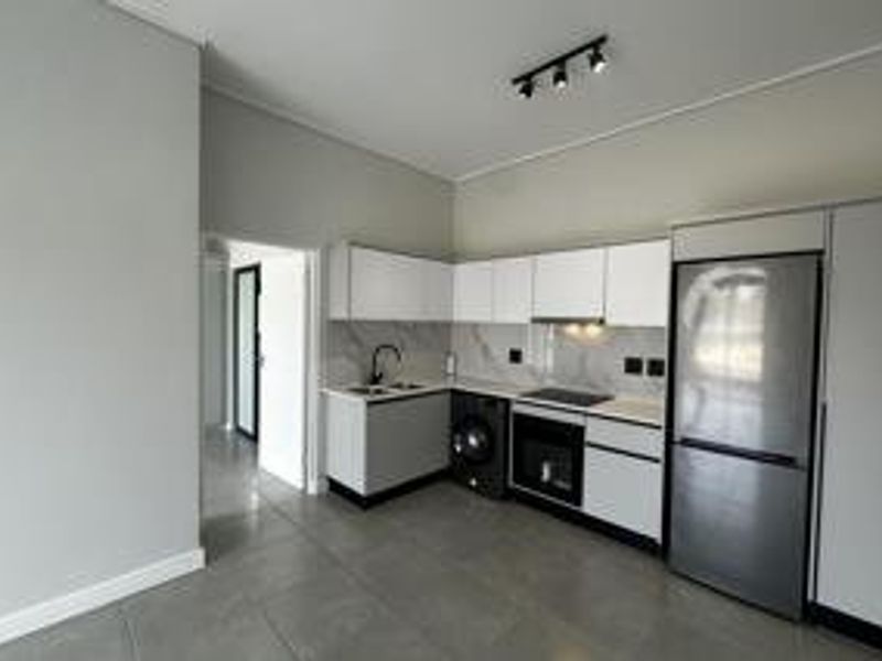 Modern, minimalist kitchen featuring sleek white cabinetry, stone countertops, integrated appliances, and contemporary track lighting in an open-plan layout.