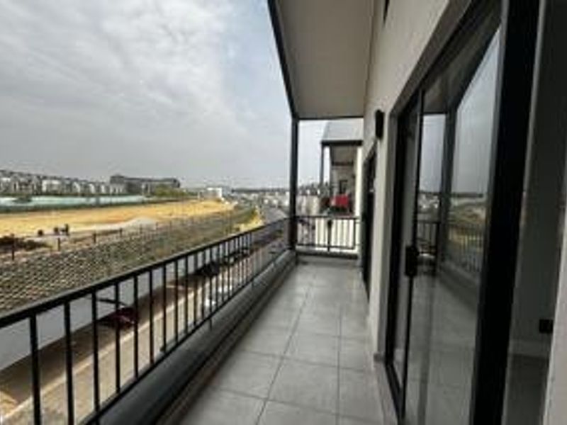 A modern, covered balcony featuring tiled flooring and a metal railing, offering an expansive view of the surrounding area.