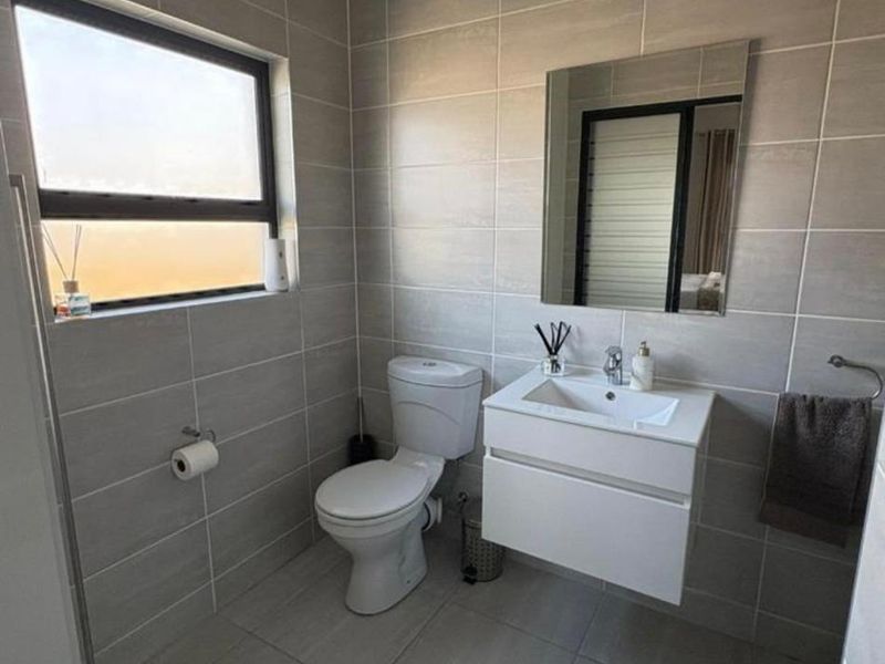 A modern, well-maintained bathroom featuring neutral floor-to-ceiling tiling, a wall-mounted vanity, and a clean, contemporary layout.