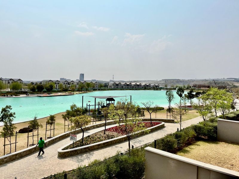 A scenic elevated view overlooking a large turquoise man-made lagoon, landscaped pathways, and surrounding residential estate infrastructure.