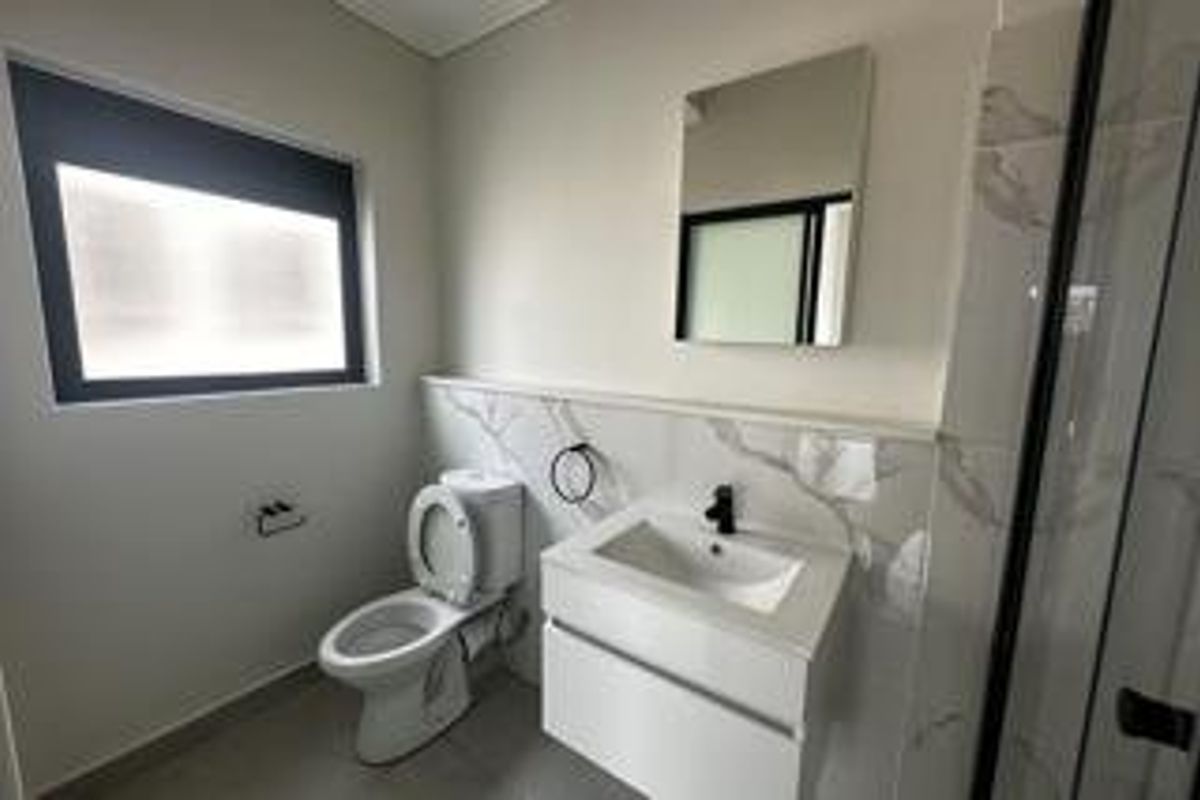 A modern, well-maintained bathroom featuring a wall-mounted vanity, ceramic basin, toilet, and a glass-enclosed shower with contemporary tiled finishes.