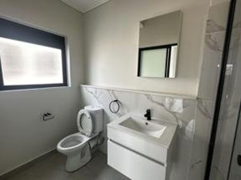 A modern, well-maintained bathroom featuring a wall-mounted vanity, ceramic basin, toilet, and a glass-enclosed shower with contemporary tiled finishes.