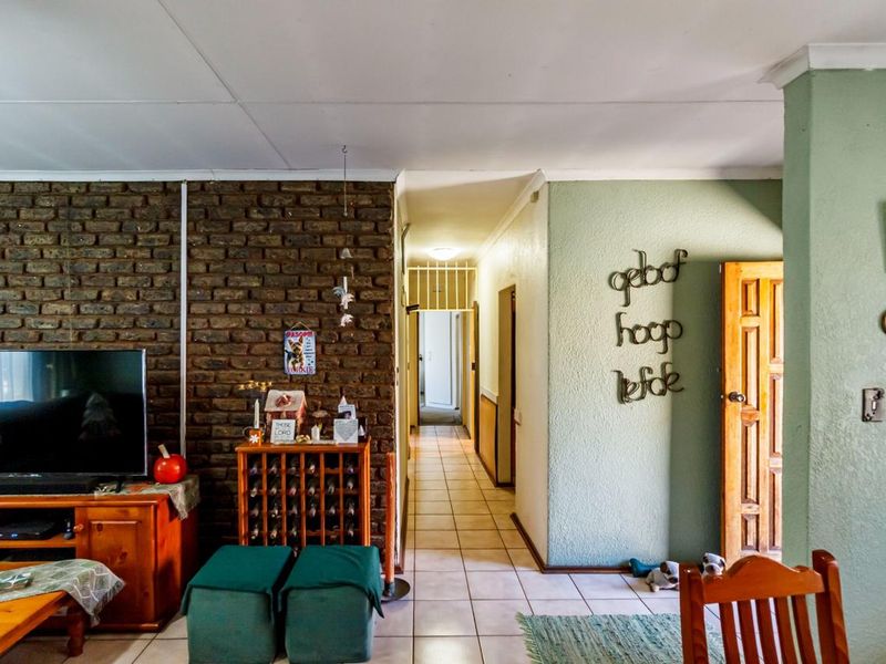 Living area featuring an exposed brick wall, tiled flooring, and a hallway leading to the rest of the home.