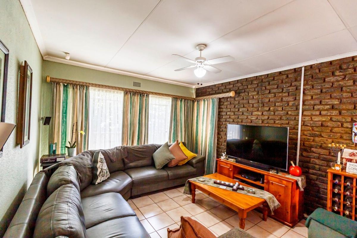 A cozy living room featuring an exposed brick accent wall, tiled flooring, and a ceiling fan, offering a warm and inviting atmosphere.
