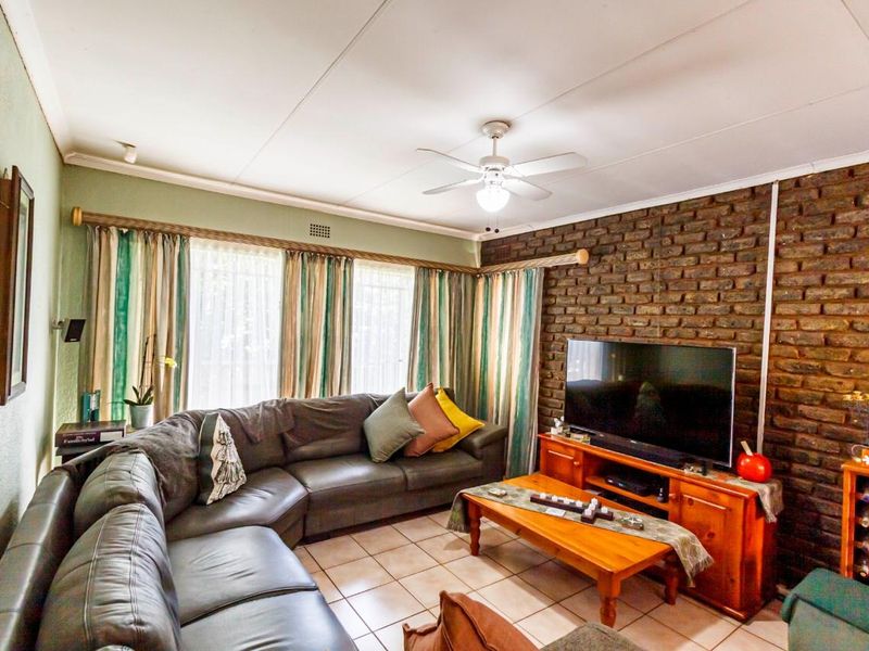 A cozy living room featuring an exposed brick accent wall, tiled flooring, and a ceiling fan, offering a warm and inviting atmosphere.