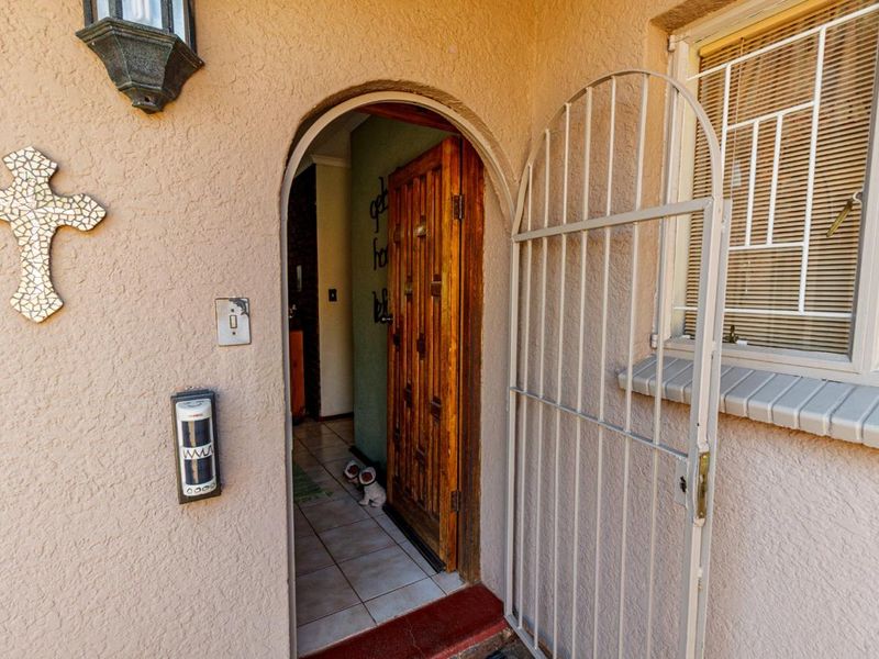 Entrance area featuring an arched doorway, a solid wooden front door, and a protective security gate, leading into a tiled interior space.