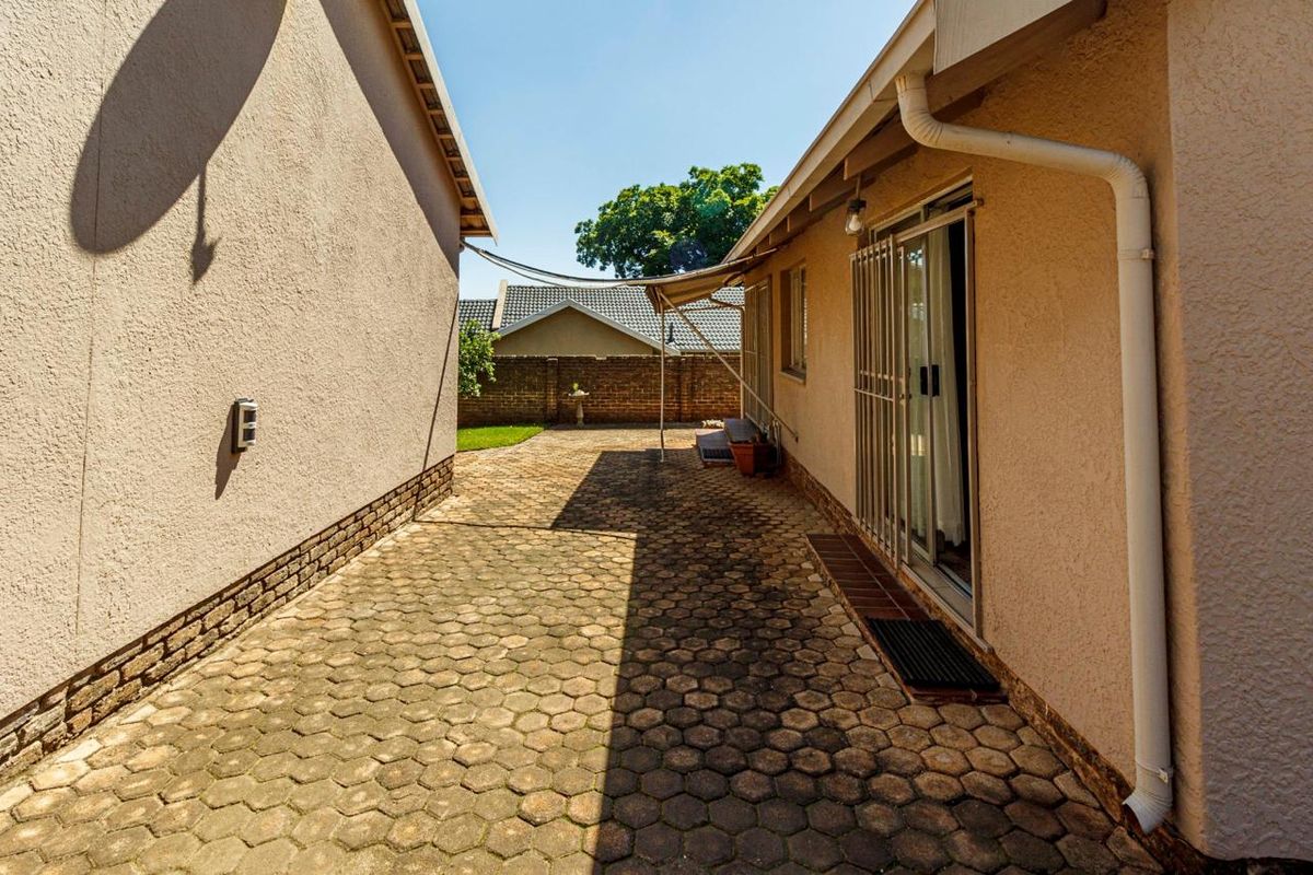 A paved side walkway and rear exterior area featuring a sliding glass door with security gate and brick boundary walling.