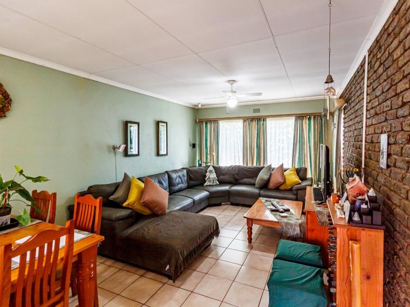 Open plan living and dining area featuring a prominent exposed brick wall, tiled flooring, and a ceiling fan.