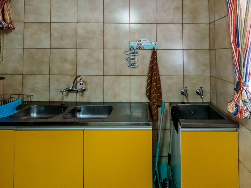 A functional laundry area featuring dual stainless steel sink units, tiled wall finishes, and built-in yellow cabinetry providing ample storage space.