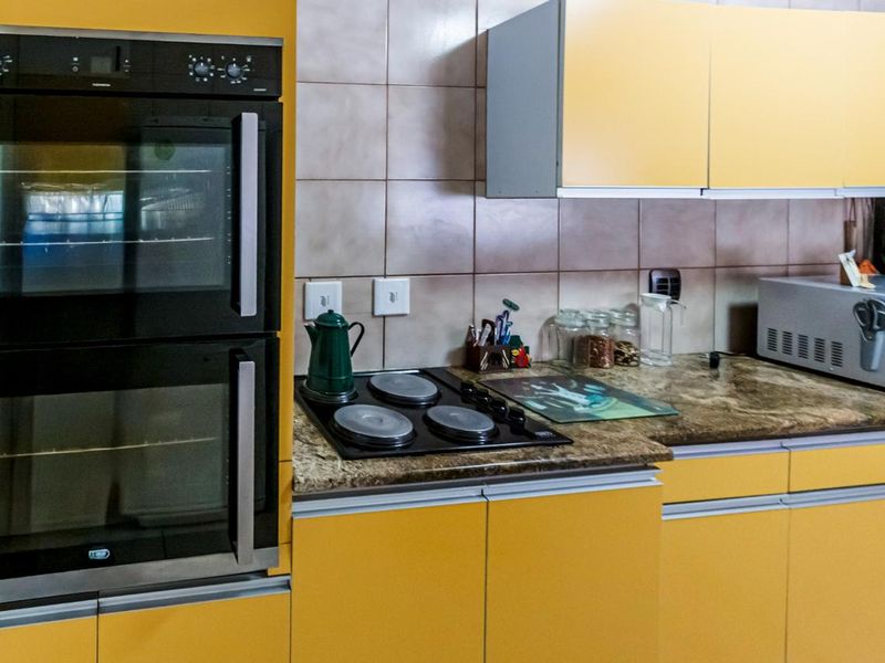A functional kitchen featuring bright yellow cabinetry, a built-in double oven, electric hob, and tiled backsplash with durable laminate countertops.
