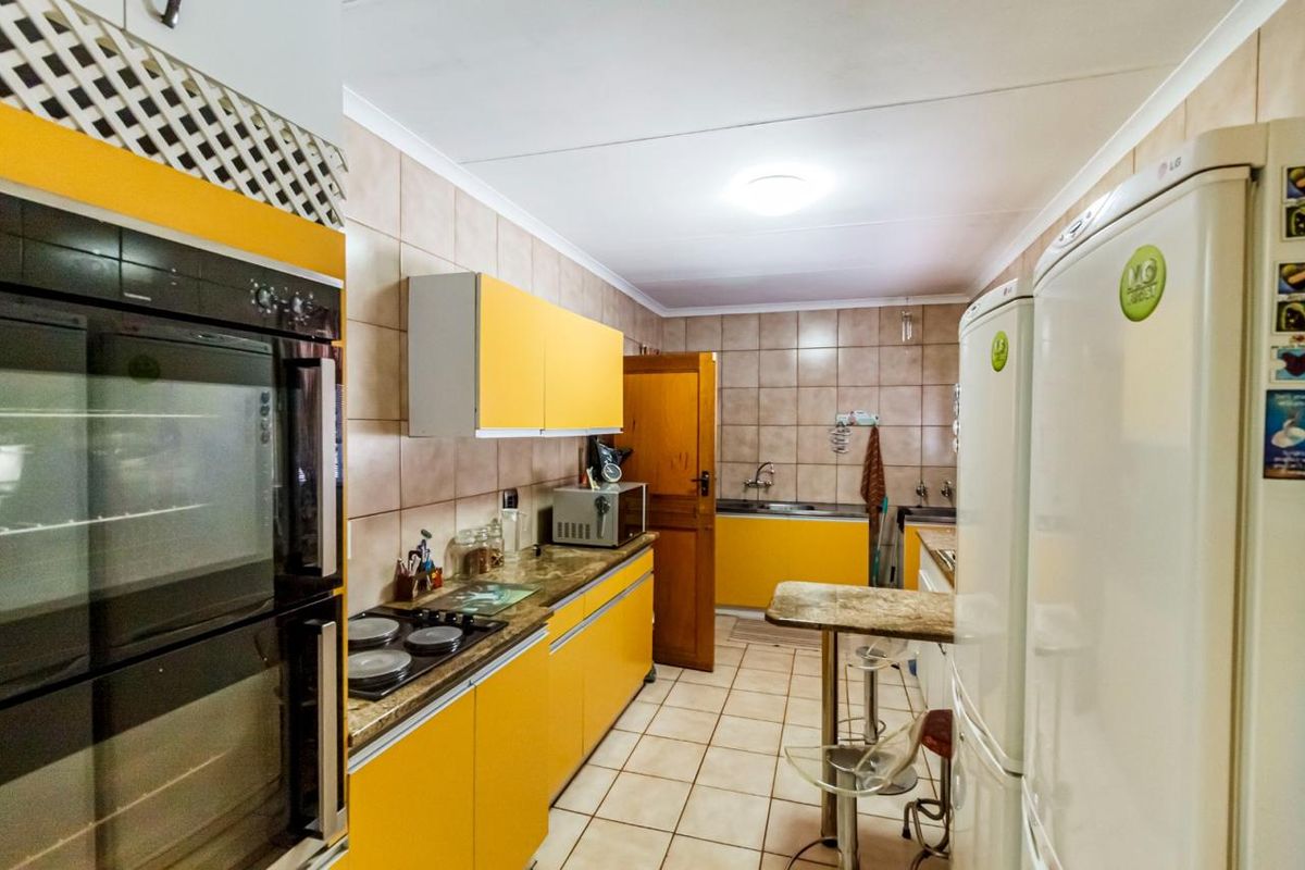 A functional kitchen featuring bright yellow cabinetry, built-in oven, electric hob, tiled backsplash, and tiled flooring with a breakfast bar area.