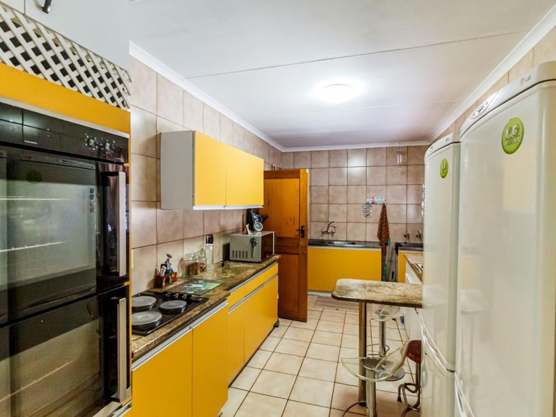 A functional kitchen featuring bright yellow cabinetry, built-in oven, electric hob, tiled backsplash, and tiled flooring with a breakfast bar area.
