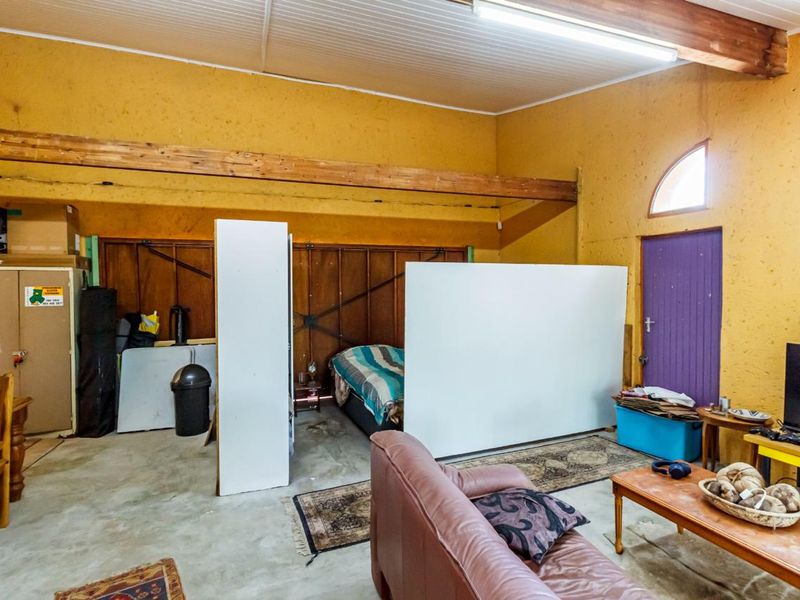 A spacious garage area featuring exposed timber beams, concrete flooring, and an arched window, currently utilized as a multi-purpose living and sleeping space.