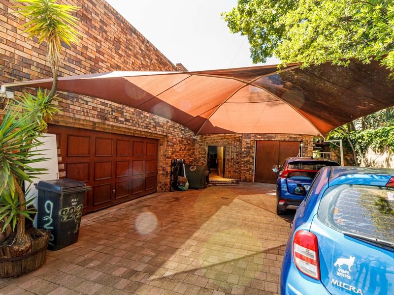 Front exterior view featuring a brick facade, paved driveway, and a large shade sail covering the parking area.