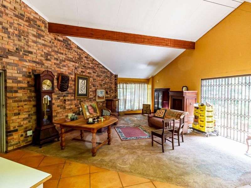 Spacious living room featuring a vaulted ceiling with exposed timber beams, a prominent exposed brick feature wall, and terracotta flooring.