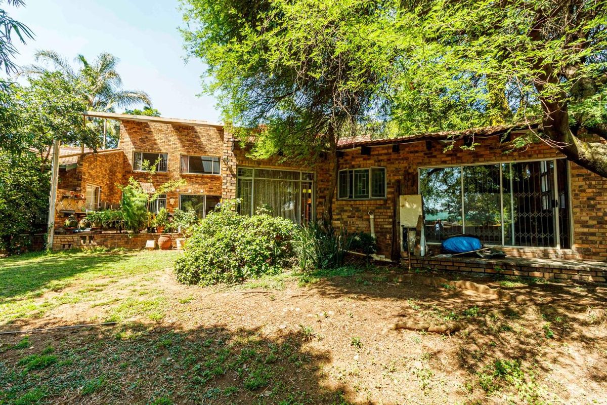 Rear view of a face brick house featuring large sliding glass doors, security gates, and a spacious garden with mature trees.
