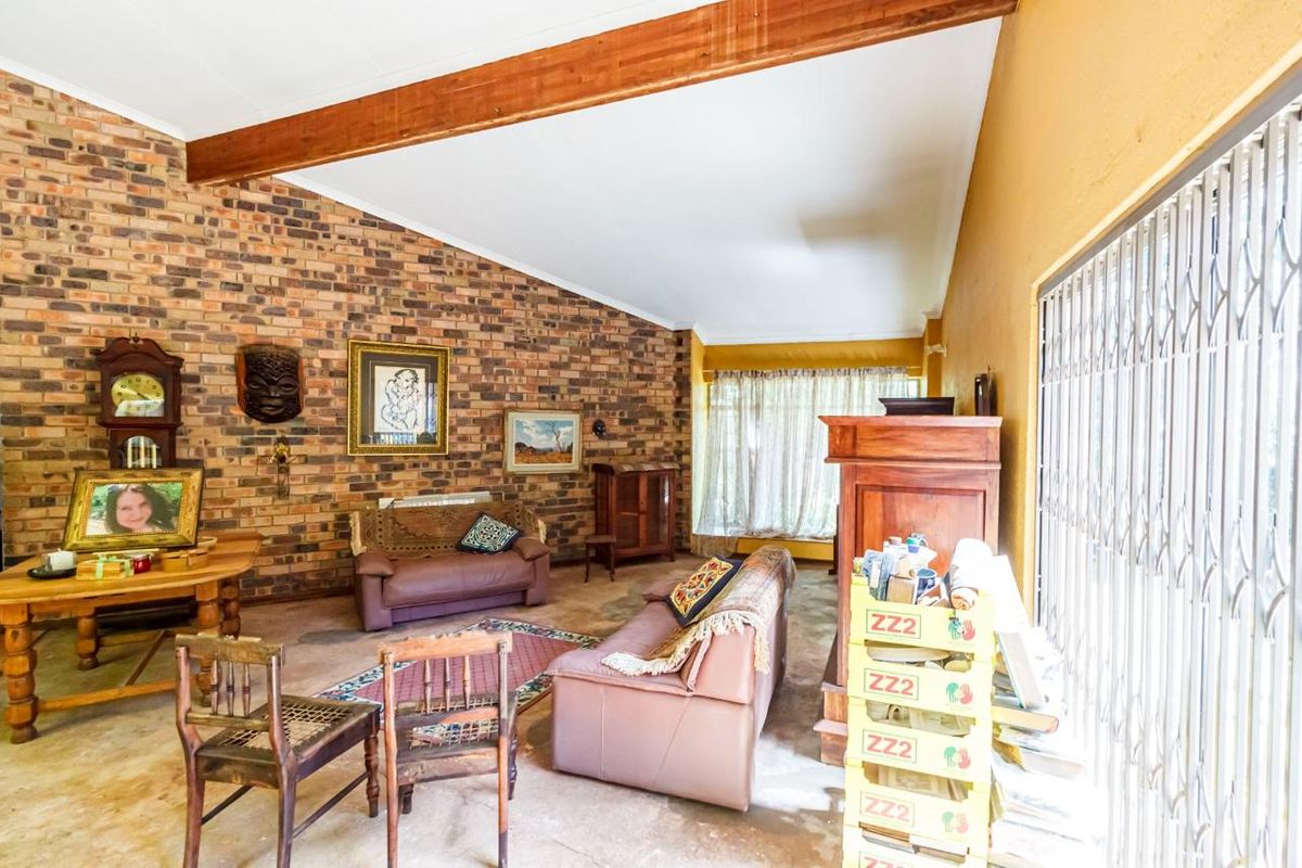 Spacious living room featuring a vaulted ceiling with exposed timber beams and a prominent face-brick feature wall, offering potential for modern renovation.